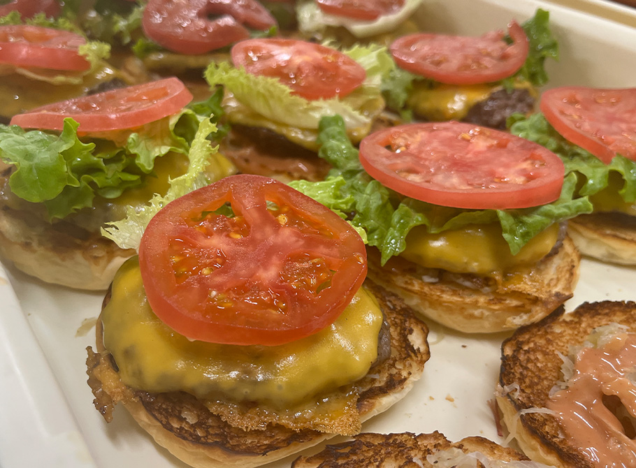 下のバンズの上にパティ、チーズ、トマトの順に乗っている作りかけのハンバーガーが複数並んでいる